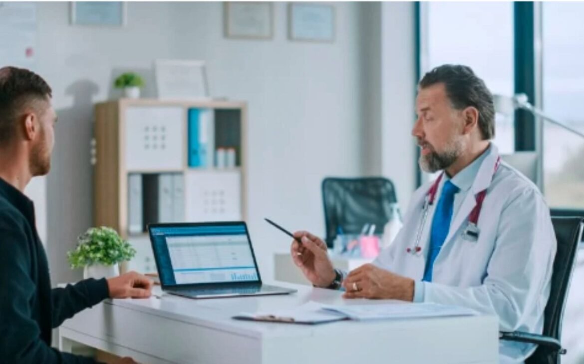 A doctor discusses information on a laptop with a male patient in a well-lit medical office using a HIPAA compliant chat.