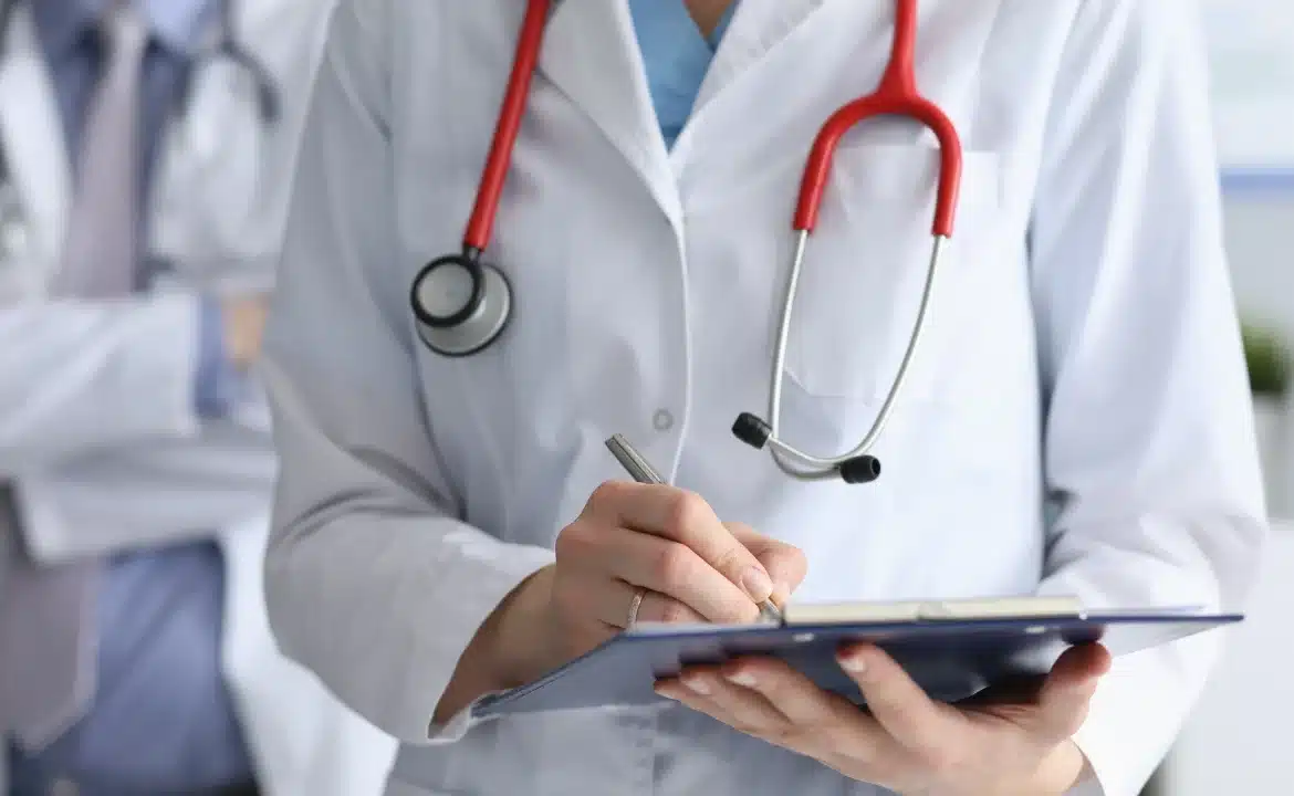 A doctor writes on a clipboard, focusing on automated prior authorization paperwork.